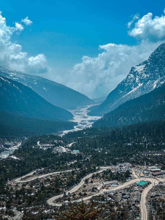 Breathtaking aerial view of Yumthang Valley's snow-capped mountains and serpentine roads.