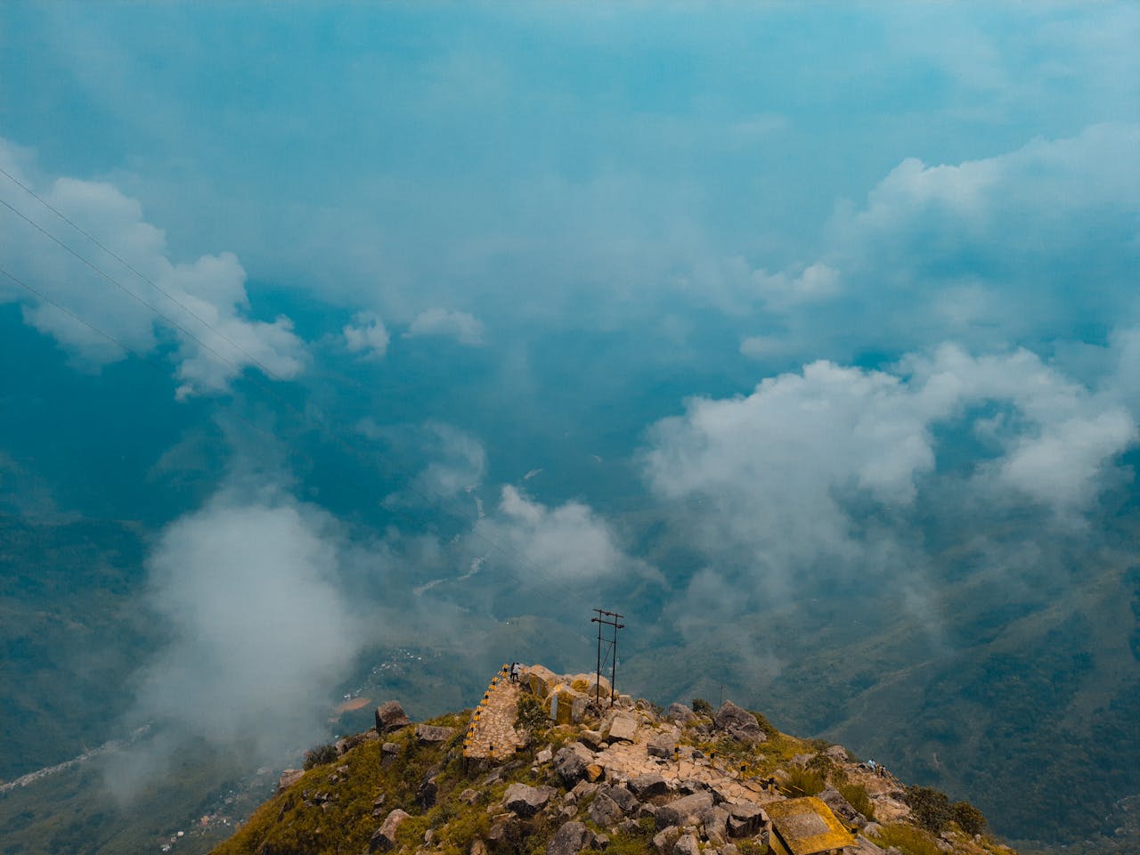 High-angle view of a rocky mountain summit surrounded by clouds in a lush green valley.